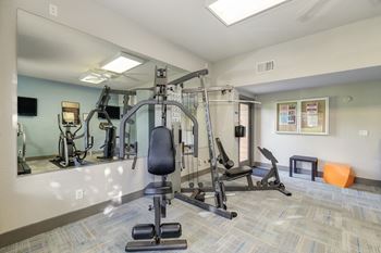 Community Fitness Center.  The Room has a light blue accent wall and contains a weight system, elliptical machines, bench and free weights.at Fountains of Fair Oaks, Fair Oaks California